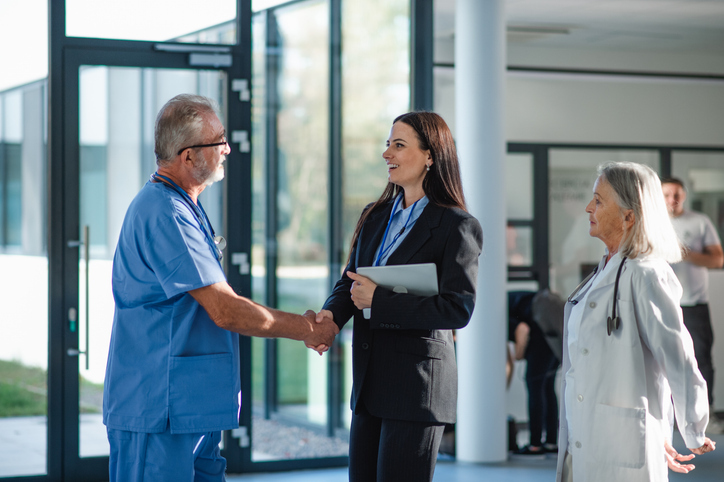 Medical person in blue scrubs shaking hands with woman in proper business attire